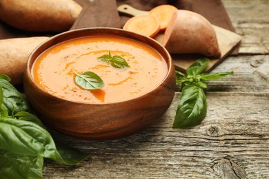 Photo of Delicious sweet potato soup, fresh vegetables and basil on wooden table, closeup