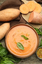 Photo of Delicious sweet potato soup with spices in bowl, fresh vegetables and basil on wooden table, flat lay