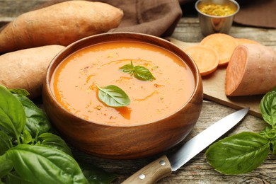 Photo of Delicious sweet potato soup, fresh vegetables, basil and knife on wooden table, closeup