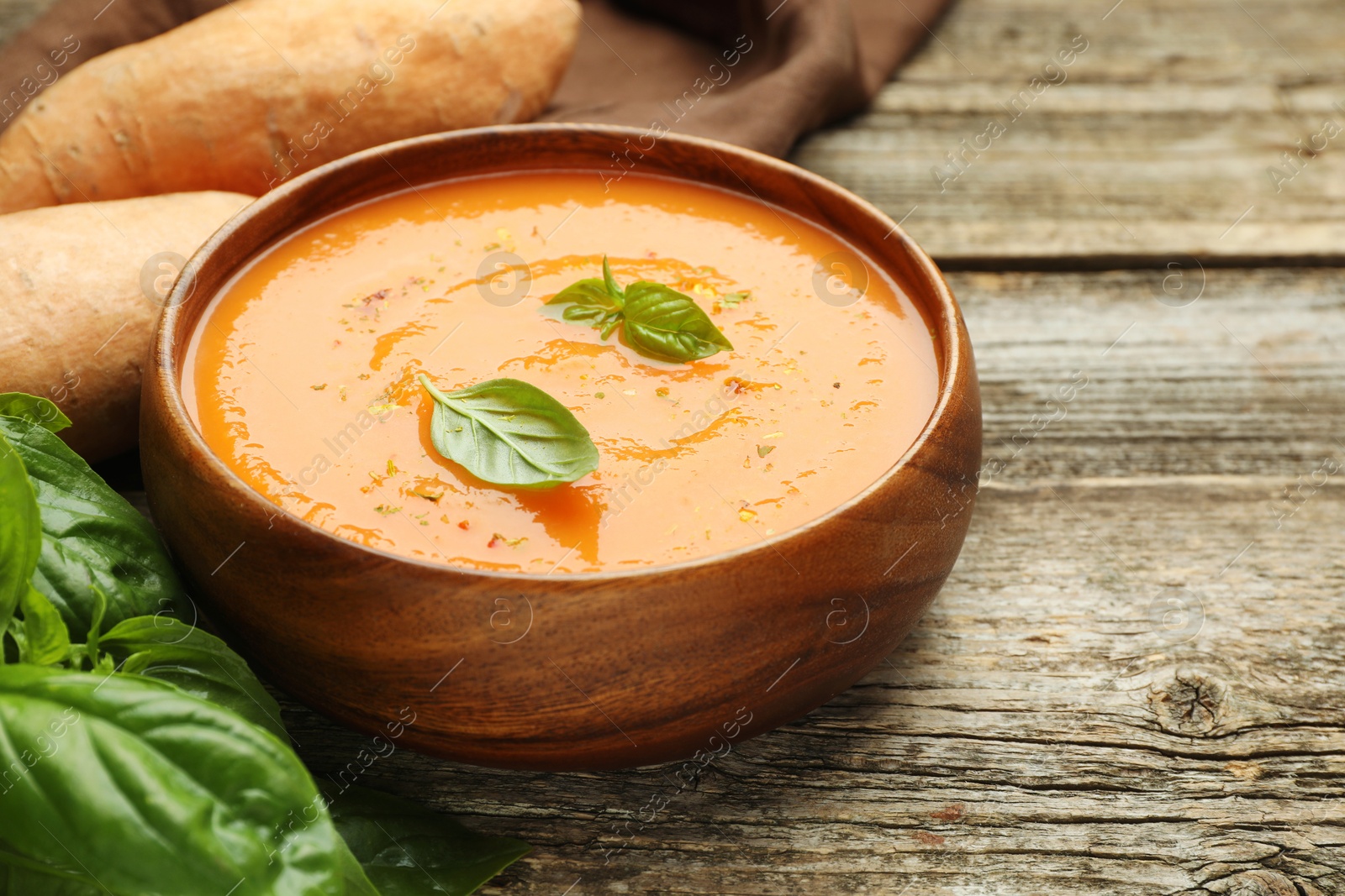 Photo of Delicious sweet potato soup, fresh vegetables and basil on wooden table, closeup