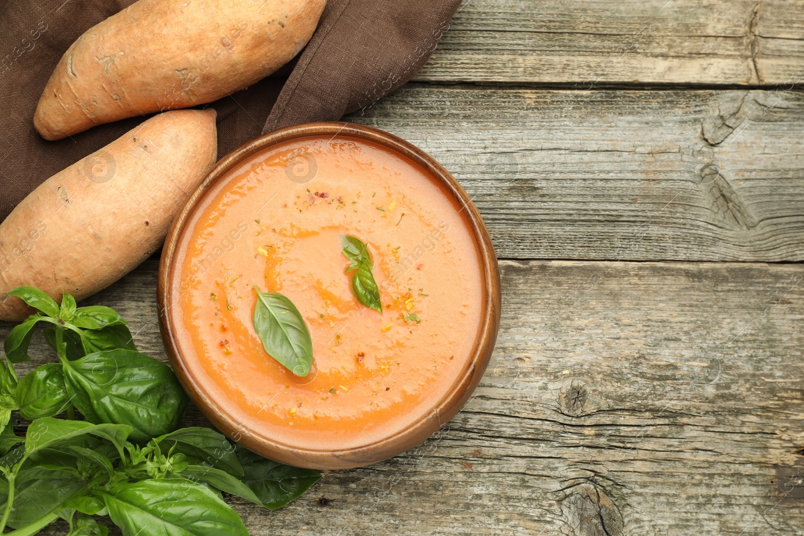 Delicious sweet potato soup with spices in bowl, fresh vegetables and basil on wooden table, flat lay. Space for text Photo of Delicious sweet potato soup with spices in bowl, fresh vegetables and basil on wooden table, flat lay. Space for text