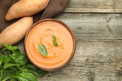 Photo of Delicious sweet potato soup with spices in bowl, fresh vegetables and basil on wooden table, flat lay. Space for text