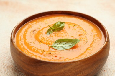 Photo of Delicious sweet potato soup with spices and basil in bowl on beige table, closeup