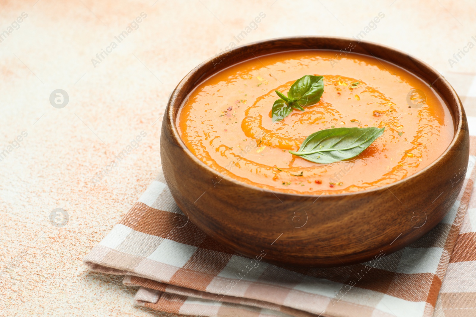 Photo of Delicious sweet potato soup with spices and basil in bowl on beige textured table, closeup