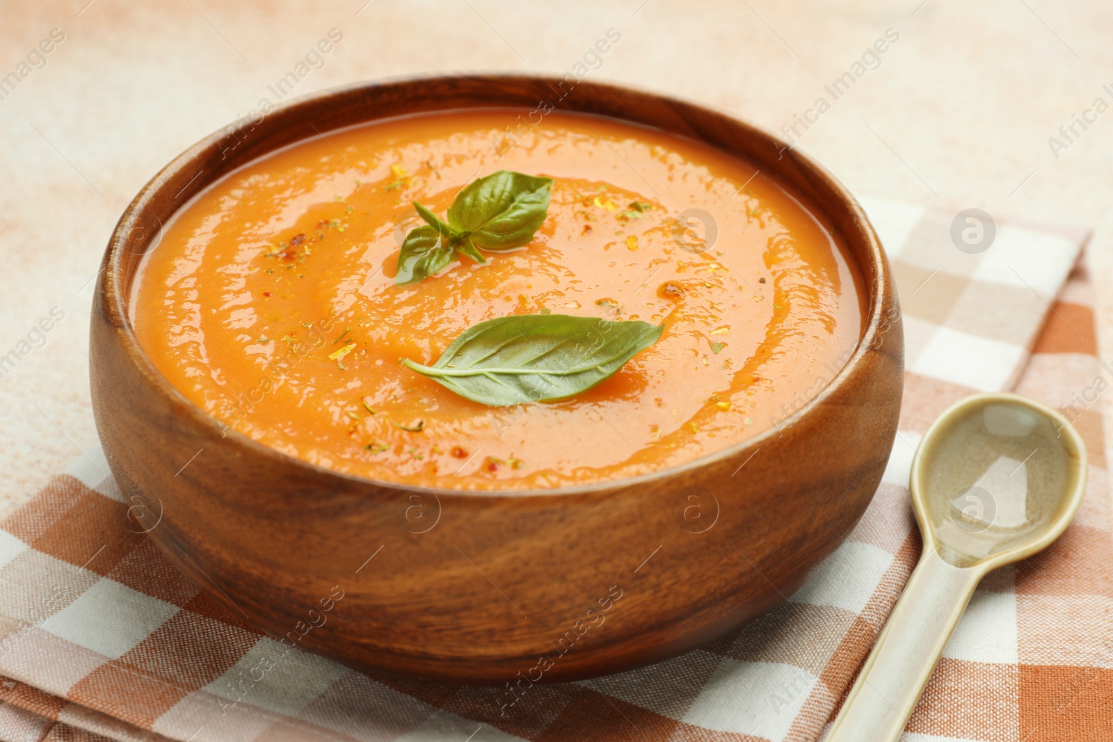 Photo of Delicious sweet potato soup with spices and basil in bowl on beige table, closeup