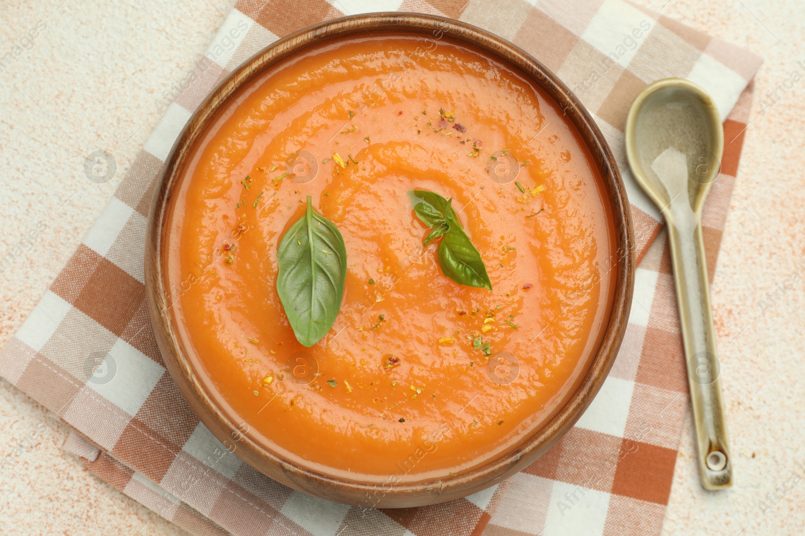 Photo of Delicious sweet potato soup with spices and basil on beige textured table, top view