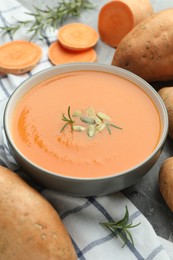 Photo of Delicious sweet potato soup with pumpkin seeds in bowl, vegetables and rosemary on table, closeup