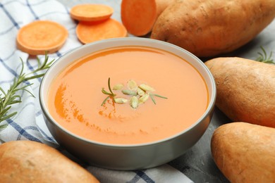 Photo of Delicious sweet potato soup with pumpkin seeds in bowl, vegetables and rosemary on table, closeup