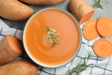 Photo of Delicious sweet potato soup with pumpkin seeds in bowl, vegetables and rosemary on grey table, flat lay