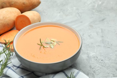 Photo of Delicious sweet potato soup with pumpkin seeds in bowl, vegetables and rosemary on grey textured table, closeup. Space for text