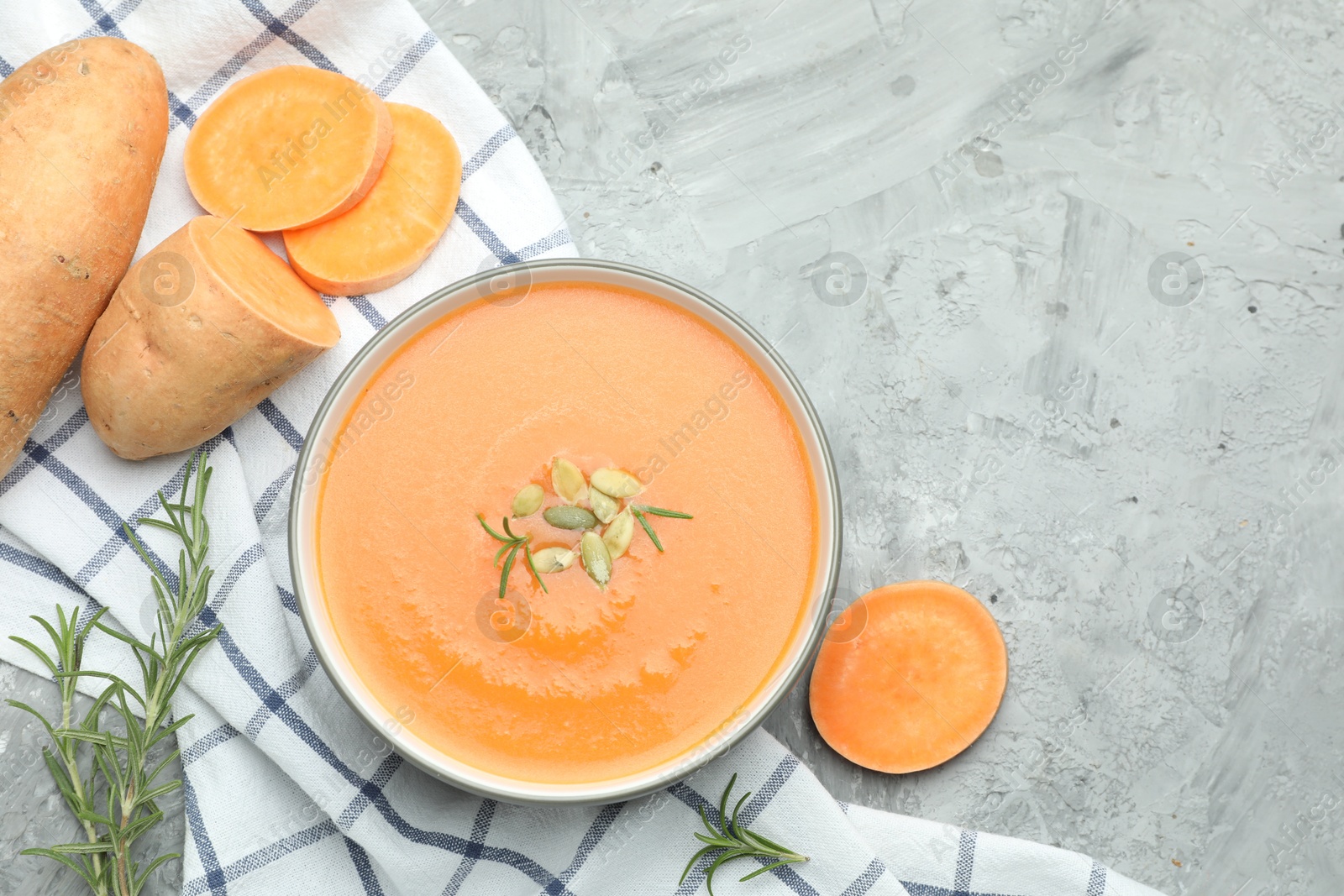 Photo of Delicious sweet potato soup with pumpkin seeds in bowl, vegetables and rosemary on grey textured table, flat lay. Space for text