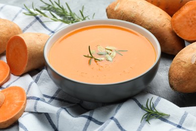 Photo of Delicious sweet potato soup with pumpkin seeds in bowl, vegetables and rosemary on table, closeup