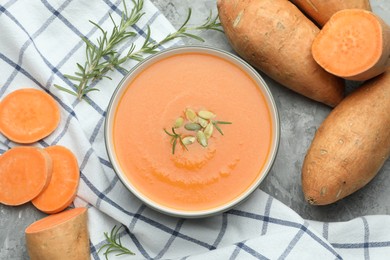 Photo of Delicious sweet potato soup with pumpkin seeds in bowl, vegetables and rosemary on grey textured table, flat lay