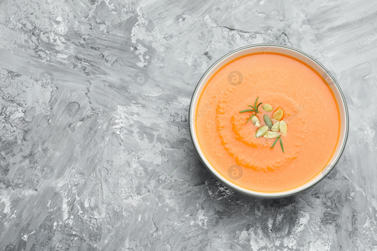 Photo of Delicious sweet potato soup with pumpkin seeds on grey textured table, top view. Space for text