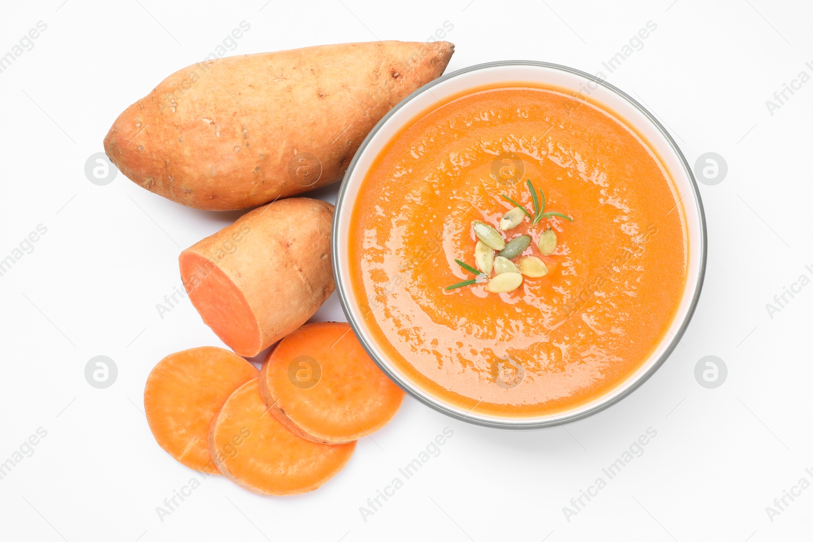 Photo of Delicious sweet potato soup with pumpkin seeds in bowl and fresh vegetables isolated on white, top view