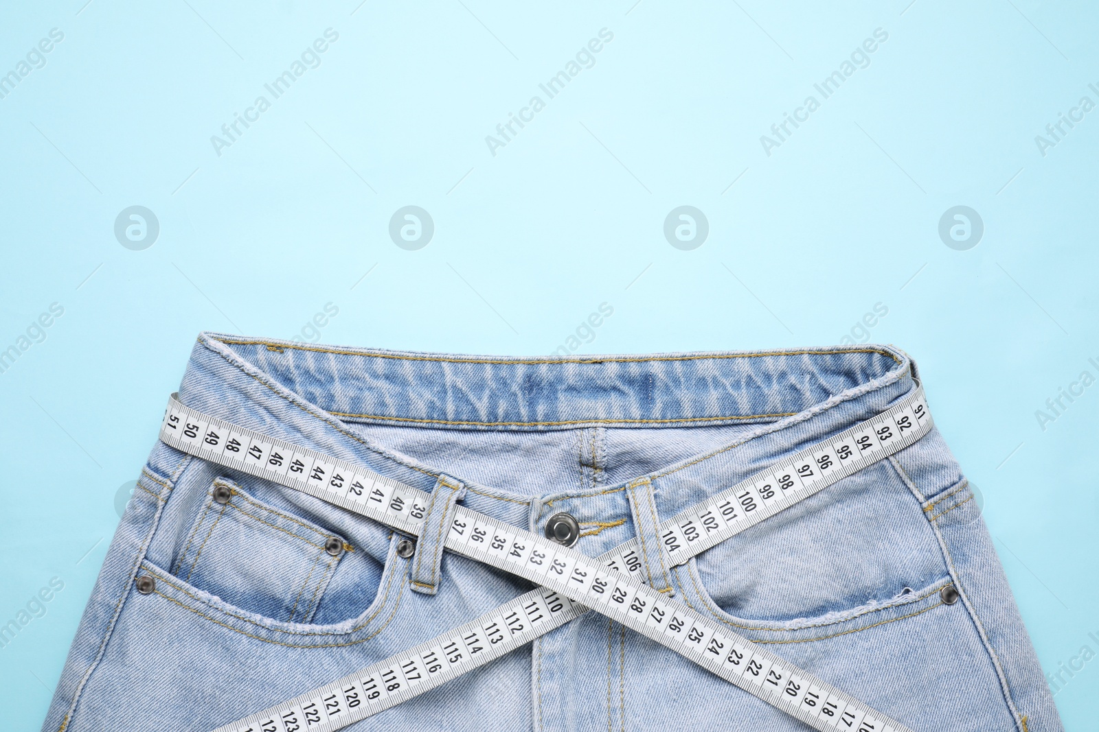 Photo of Jeans and measuring tape on light blue background, top view