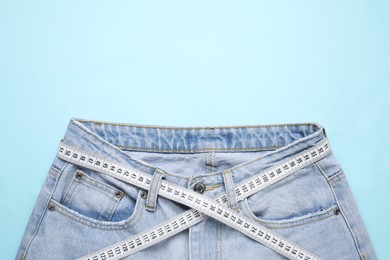 Photo of Jeans and measuring tape on light blue background, top view