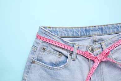 Photo of Jeans and measuring tape on light blue background, top view