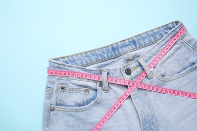 Photo of Jeans and measuring tape on light blue background, top view