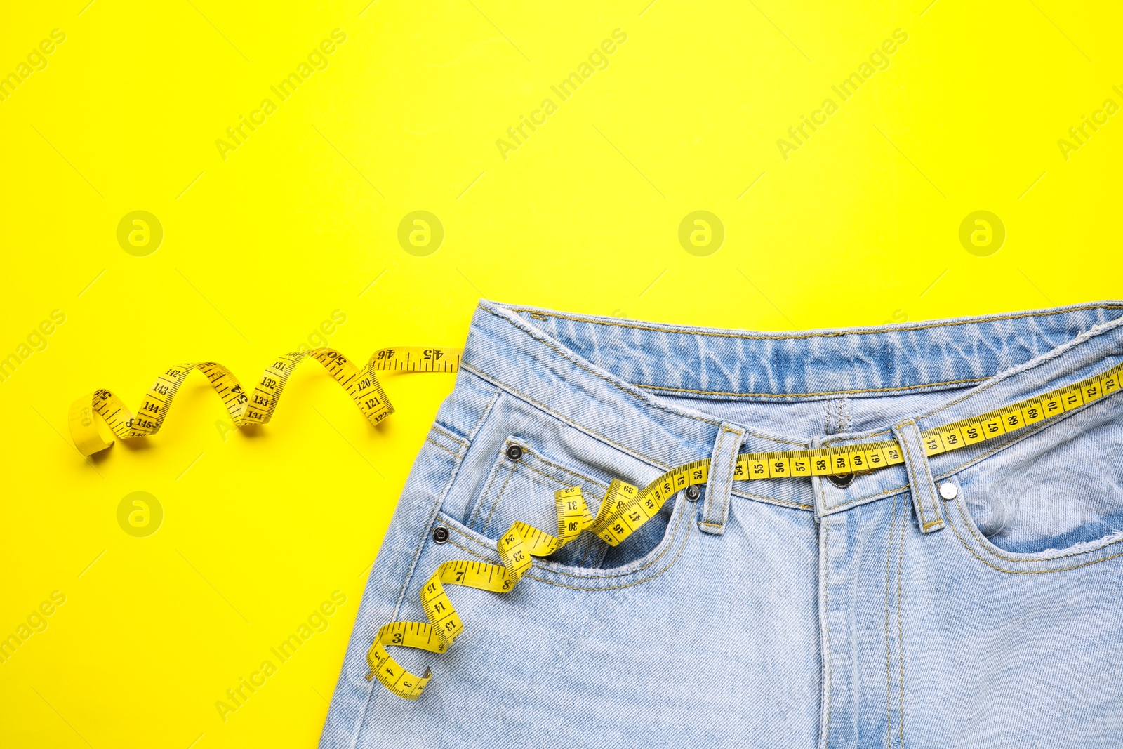 Photo of Jeans and measuring tape on yellow background, top view