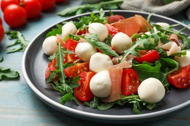 Photo of Tasty salad with arugula, mozzarella cheese, tomatoes and jamon on light blue wooden table, closeup