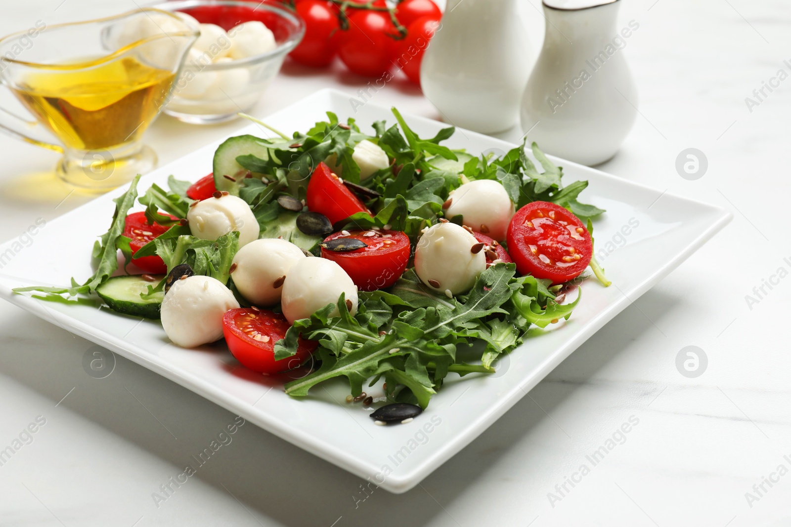 Photo of Tasty salad with arugula, mozzarella cheese and vegetables on white table, closeup