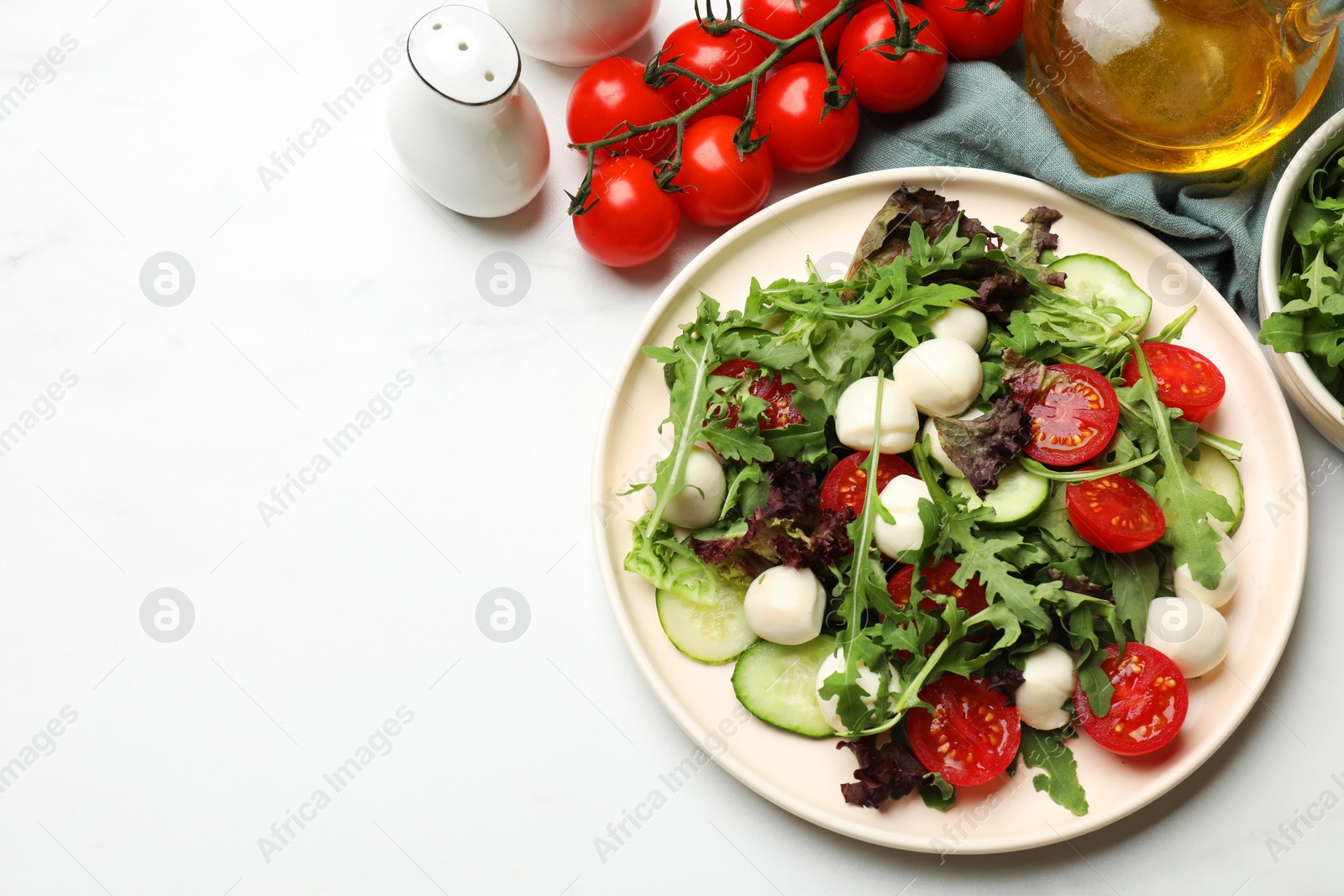 Photo of Tasty salad with arugula, lettuce, mozzarella cheese and vegetables on white table, flat lay. Space for text