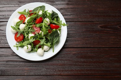 Photo of Tasty salad with arugula, spinach, mozzarella cheese and tomatoes on wooden table, top view. Space for text