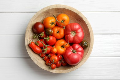 Photo of Different ripe tomatoes in bowl on white wooden table, top view