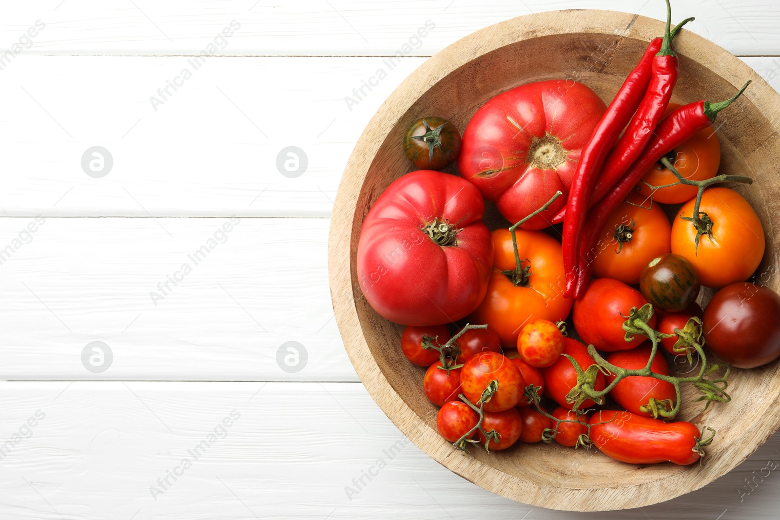 Photo of Different ripe tomatoes and chili peppers in bowl on white wooden table, top view. Space for text