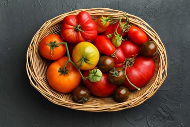 Photo of Different ripe and unripe tomatoes in wicker basket on grey textured table, top view