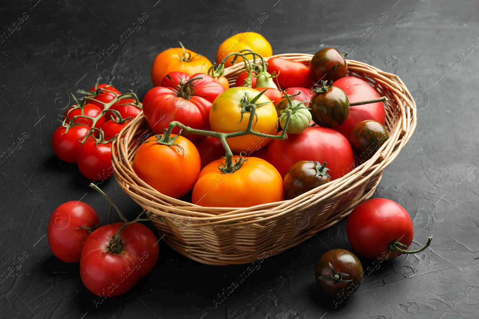 Photo of Basket with different ripe and unripe tomatoes on grey textured table