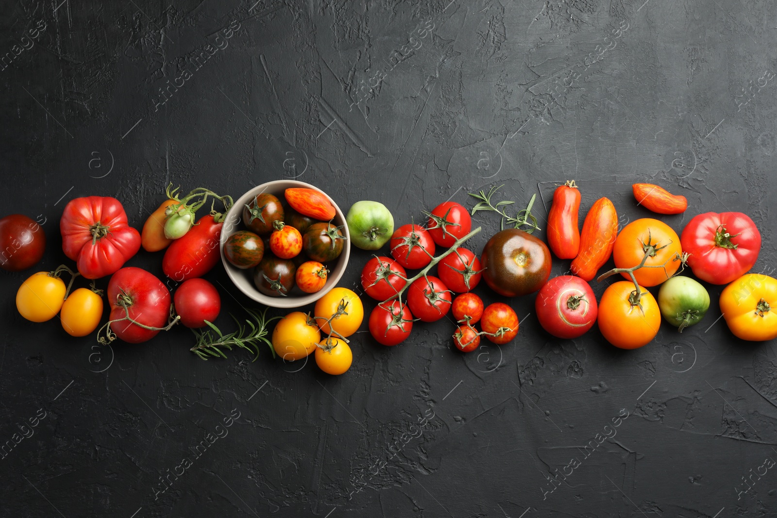 Photo of Different fresh tomatoes and rosemary on grey textured table, flat lay