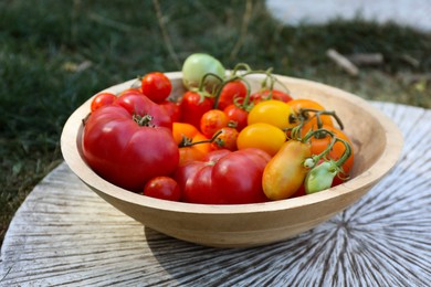 Different fresh tomatoes in bowl on wooden surface outdoors