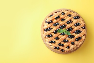 Photo of Delicious homemade blueberry pie with mint on yellow background, top view. Space for text