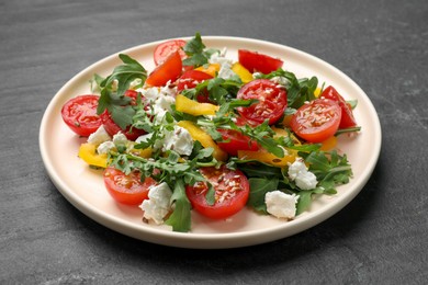 Photo of Tasty salad with arugula, cheese and vegetables on dark textured table, closeup