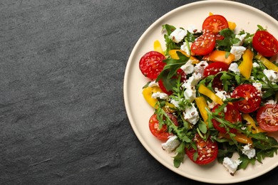 Photo of Tasty salad with arugula, cheese and vegetables on dark textured table, top view. Space for text