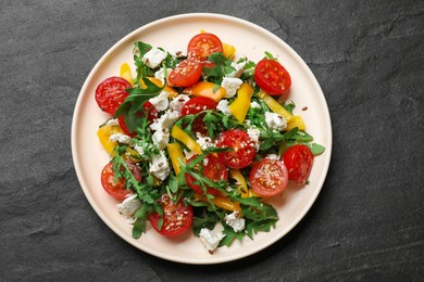 Photo of Tasty salad with arugula, cheese and vegetables on dark textured table, top view