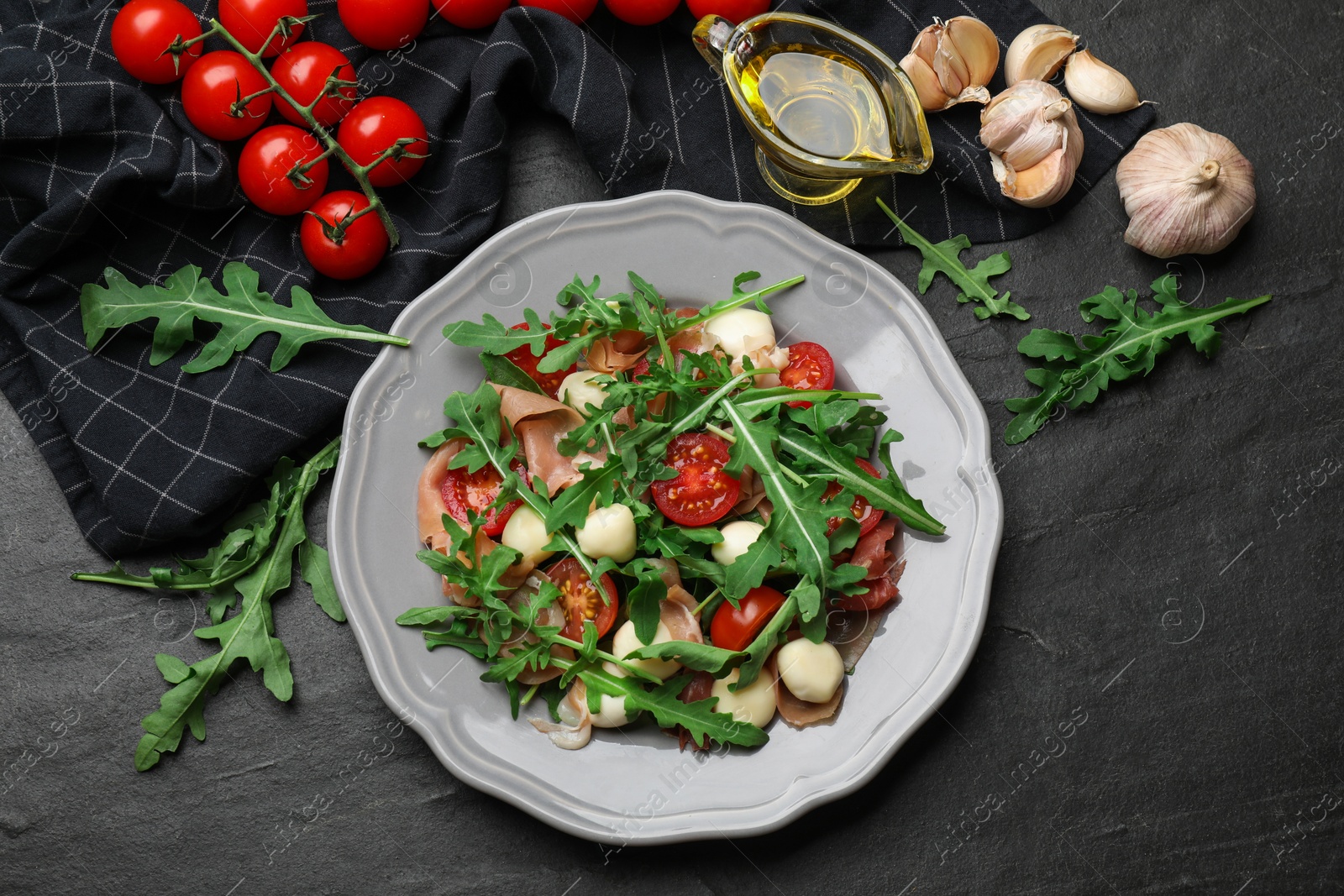 Photo of Tasty salad with arugula, cheese and vegetables on dark textured table, flat lay