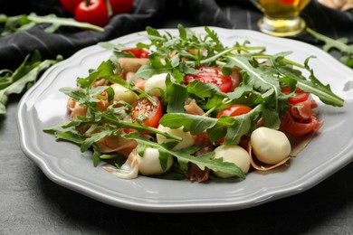 Photo of Tasty salad with arugula on dark textured table, closeup