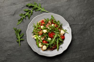 Photo of Tasty salad with arugula on dark textured table, flat lay