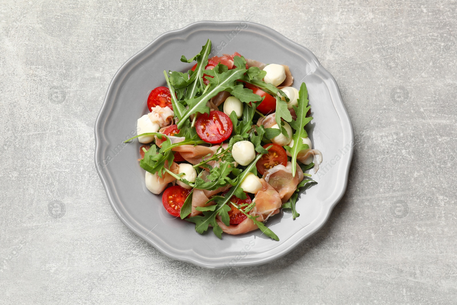 Photo of Tasty salad with arugula on grey textured table, top view