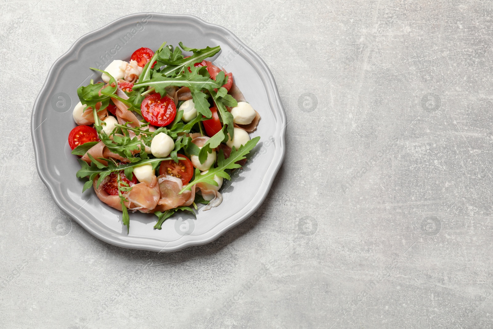 Photo of Tasty salad with arugula on grey textured table, top view. Space for text