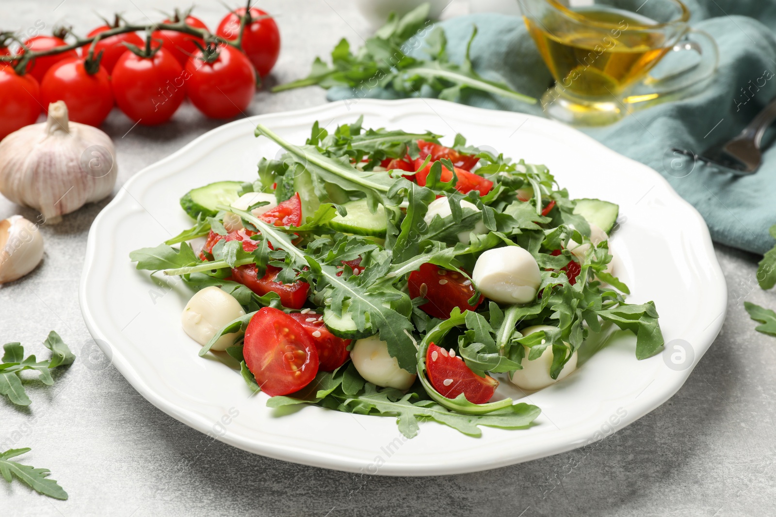 Photo of Tasty salad with arugula, mozzarella, tomatoes and cucumber on grey textured table, closeup