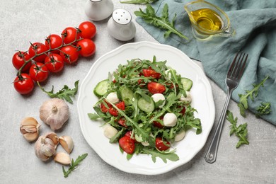 Photo of Tasty salad with arugula, mozzarella, tomatoes and cucumber served on grey textured table, flat lay