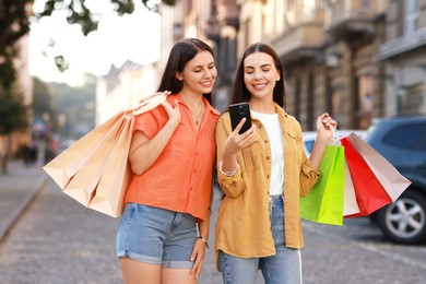 Happy women with colorful shopping bags using smartphone outdoors