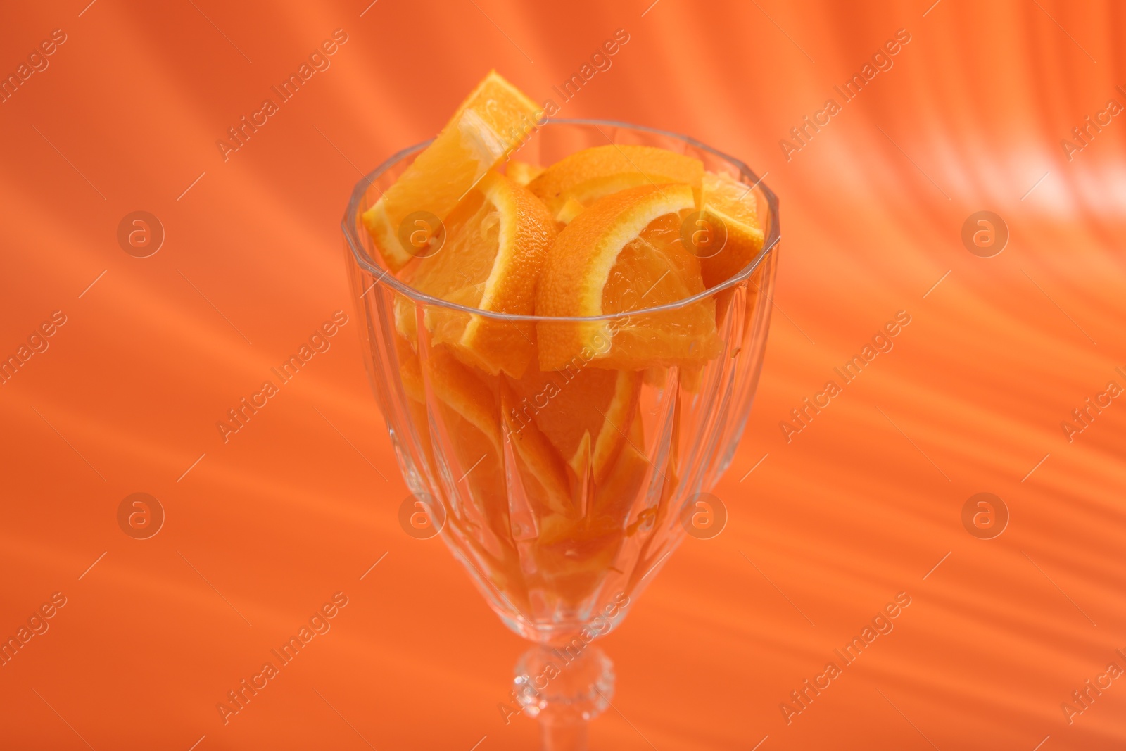 Photo of Orange slices in cocktail glass on orange background, closeup