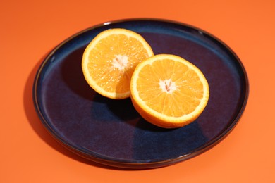 Photo of Dark blue plate with orange halves on orange background, closeup