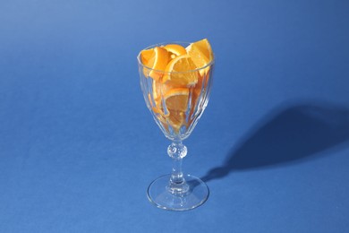 Photo of Orange slices in cocktail glass on blue background