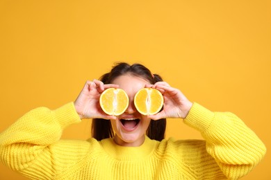 Photo of Happy girl holding orange halves near eyes on orange background